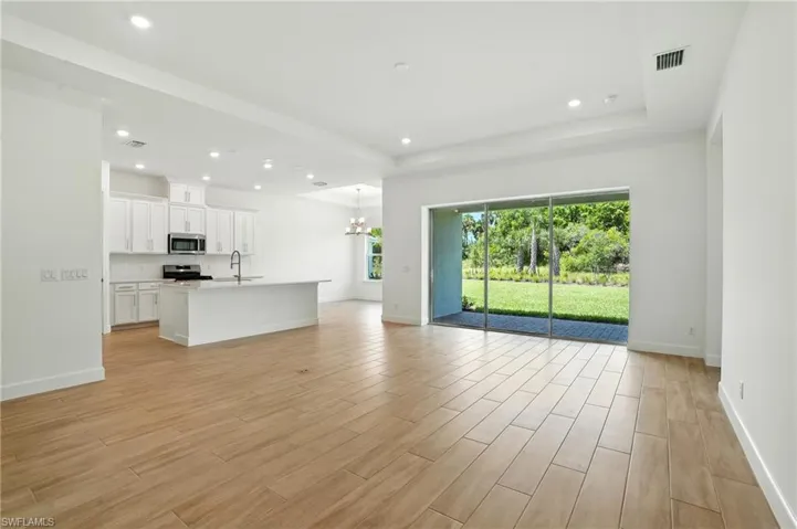 Unfurnished living room with recessed lighting, light wood-type flooring, a chandelier, and a tray ceiling