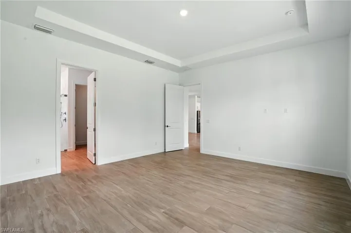 Unfurnished bedroom with light wood-type flooring, a raised ceiling, and recessed lighting