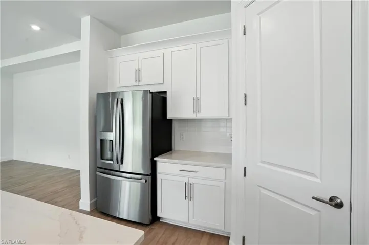 Kitchen with white cabinets, stainless steel refrigerator with ice dispenser, light wood-style flooring, decorative backsplash, and recessed lighting