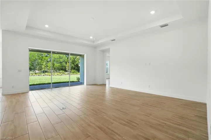 Empty room with a raised ceiling, recessed lighting, and light wood-type flooring