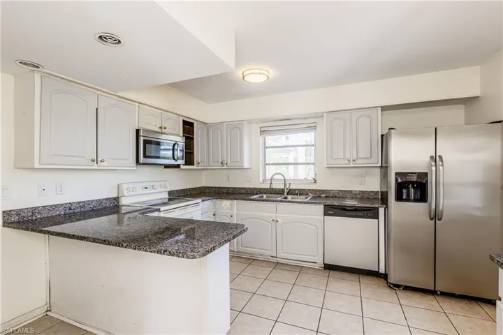 Kitchen with white cabinets, sink, appliances with stainless steel finishes, light tile patterned flooring, and kitchen peninsula