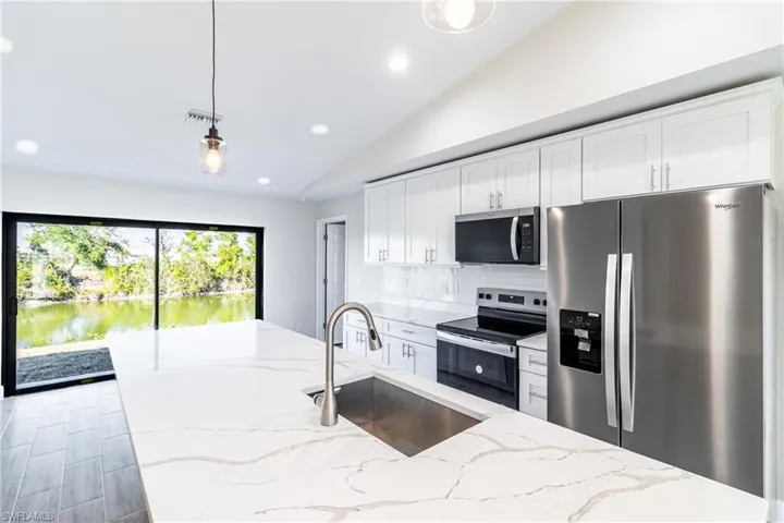 Kitchen with appliances with stainless steel finishes, white cabinetry, sink, hanging light fixtures, and light stone countertops