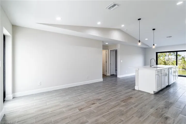 Kitchen featuring pendant lighting, lofted ceiling, sink, white cabinets, and a center island with sink