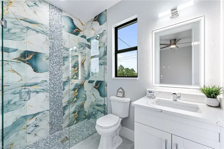 Bathroom featuring toilet, ceiling fan, an enclosed shower, and vanity