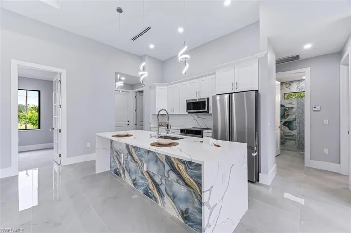 Kitchen featuring light stone countertops, white cabinetry, stainless steel appliances, decorative light fixtures, and a center island with sink