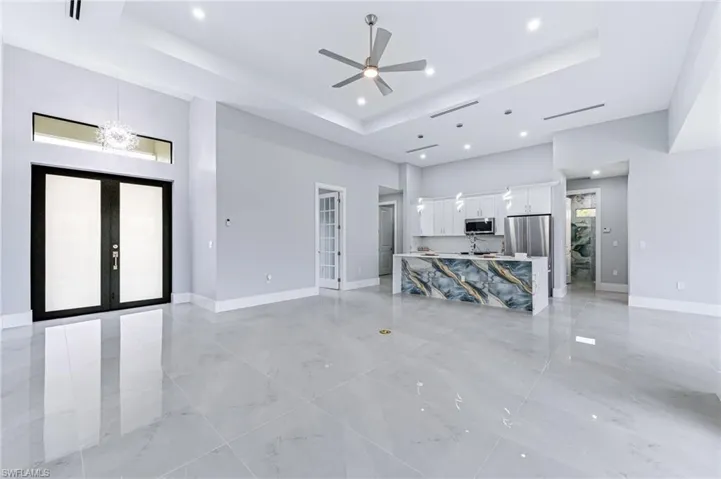 Unfurnished living room featuring ceiling fan with notable chandelier, a raised ceiling, a high ceiling, and french doors