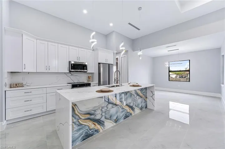 Kitchen with backsplash, stainless steel appliances, decorative light fixtures, a center island with sink, and white cabinetry