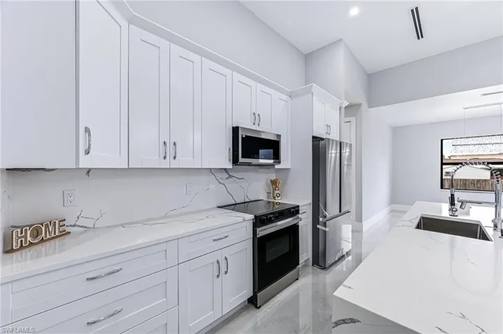 Kitchen featuring white cabinets, light stone counters, sink, and stainless steel appliances