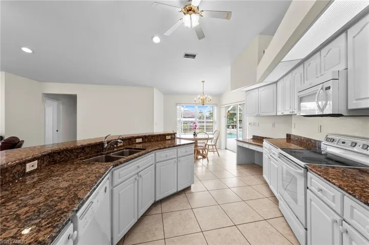 Kitchen with white appliances, light tile patterned flooring, ceiling fan, a chandelier, and dark stone counters