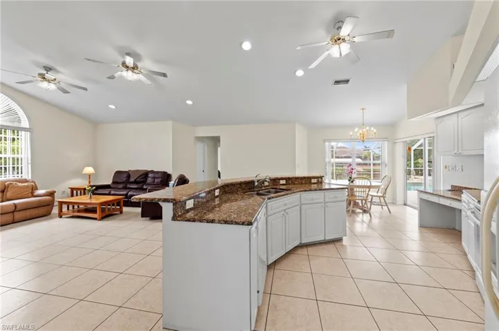 Kitchen featuring lofted ceiling, light tile patterned flooring, open floor plan, healthy amount of natural light, and a chandelier