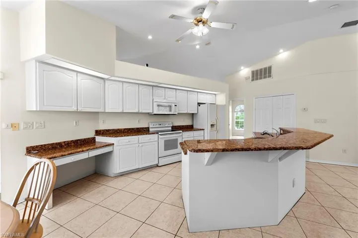 Kitchen with white appliances, high vaulted ceiling, light tile patterned flooring, white cabinets, and dark stone counters
