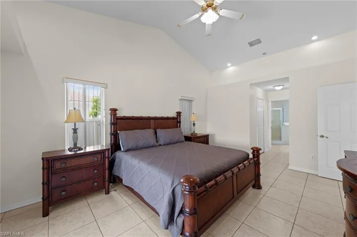Bedroom with high vaulted ceiling, light tile patterned flooring, and ensuite bath