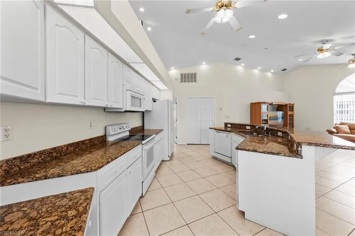 Kitchen with white appliances, a ceiling fan, vaulted ceiling, white cabinetry, and recessed lighting