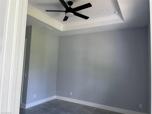 Unfurnished room with crown molding, dark tile flooring, ceiling fan, and a raised ceiling