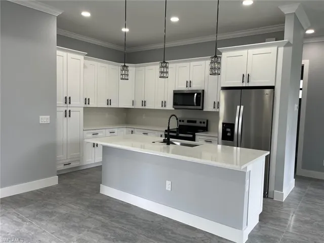 Kitchen with stainless steel appliances, sink, decorative light fixtures, a center island with sink, and white cabinetry
