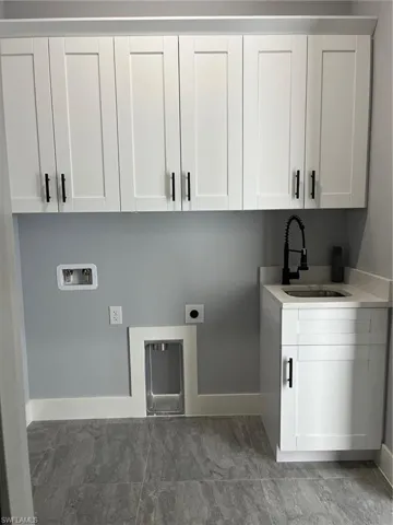 Washroom with hookup for a washing machine, sink, cabinets, hookup for an electric dryer, and light tile patterned flooring