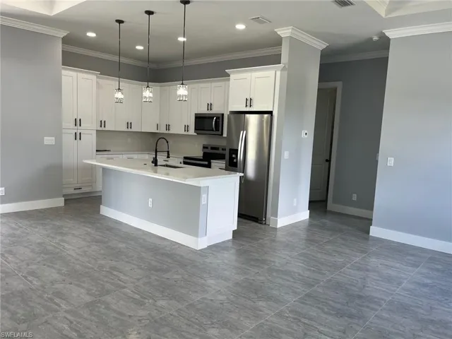 Kitchen with tile patterned flooring, hanging light fixtures, an island with sink, white cabinets, and appliances with stainless steel finishes