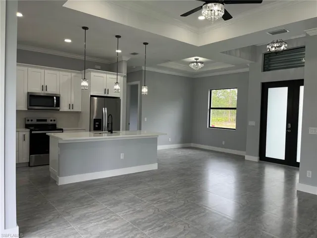 Kitchen featuring white cabinets, stainless steel appliances, a kitchen island with sink, and ornamental molding