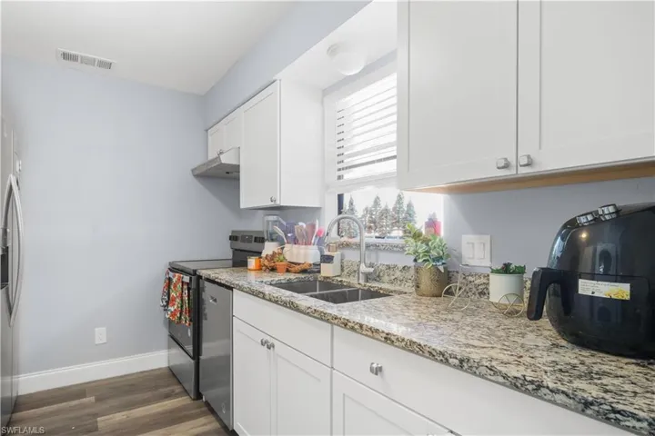 Kitchen featuring white cabinets, stainless steel appliances, light stone countertops, dark wood-style floors, and under cabinet range hood