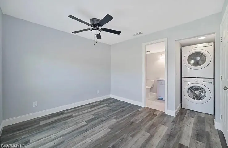 Washroom with dark wood-style floors, stacked washer / dryer, and ceiling fan