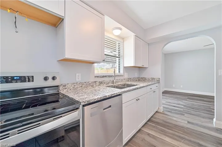 Kitchen with stainless steel appliances, white cabinets, light wood-type flooring, light stone counters, and arched walkways
