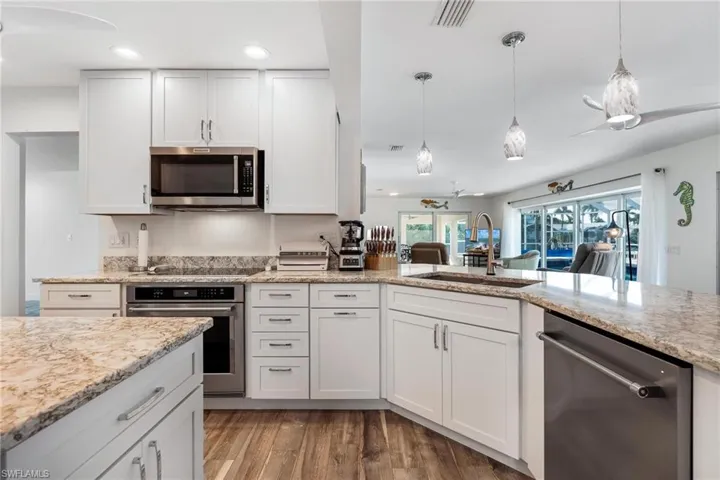 Kitchen featuring wood-type flooring, appliances with stainless steel finishes, hanging light fixtures, and white cabinetry