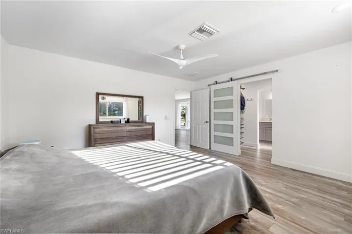 Bedroom featuring ceiling fan, ensuite bath, a barn door, and light hardwood / wood-style floors