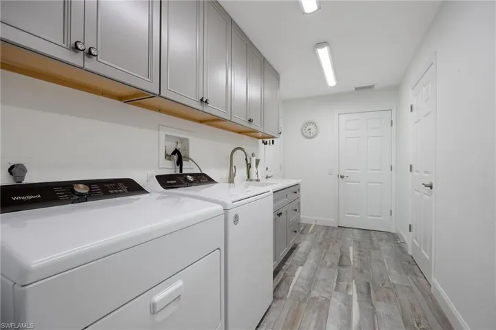 Washroom featuring cabinets, washing machine and clothes dryer, sink, and light hardwood / wood-style laminate floors