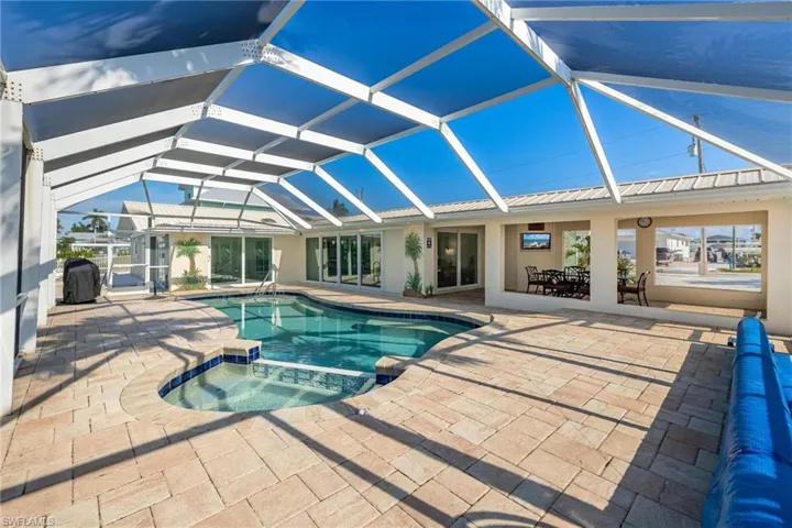 View of pool with glass enclosure, an in ground hot tub, and a patio area
