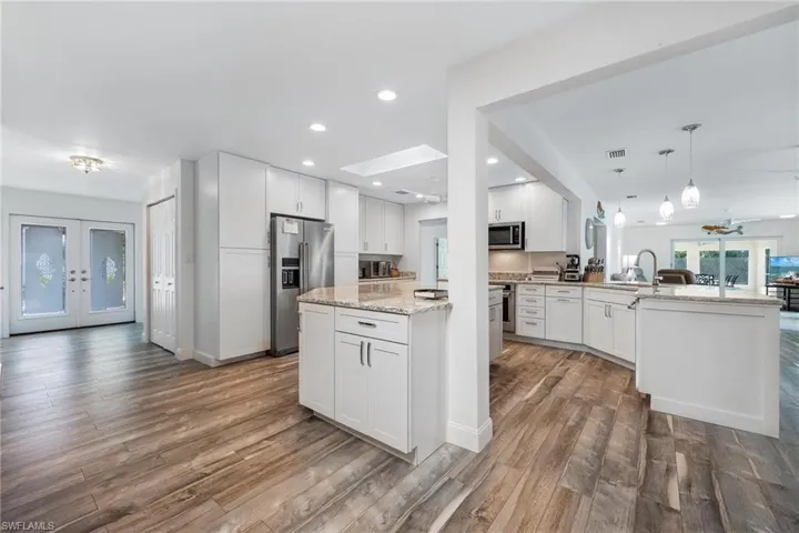 Kitchen featuring hardwood / wood-style floors, appliances with stainless steel finishes, white cabinets, ceiling fan, and light stone counters