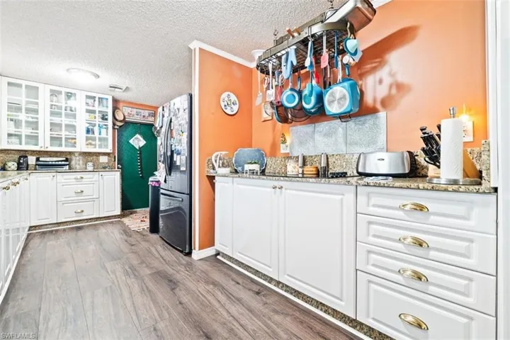 Kitchen with white cabinetry, light stone counters, freestanding refrigerator, dark wood finished floors, and glass fronted cabinets