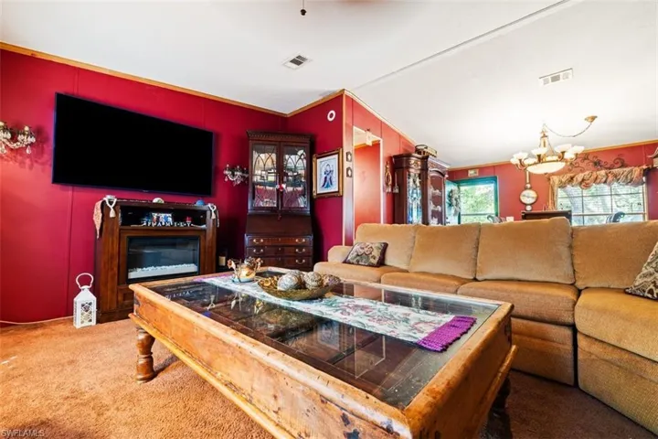 Living area featuring carpet, a chandelier, a glass covered fireplace, crown molding, and lofted ceiling