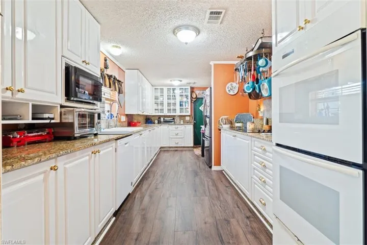 Kitchen featuring white appliances, white cabinets, dark wood-style floors, light stone counters, and glass insert cabinets
