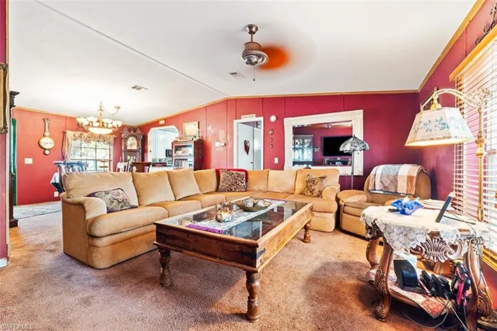 Carpeted living area featuring lofted ceiling, suspended lighting, and ceiling fan