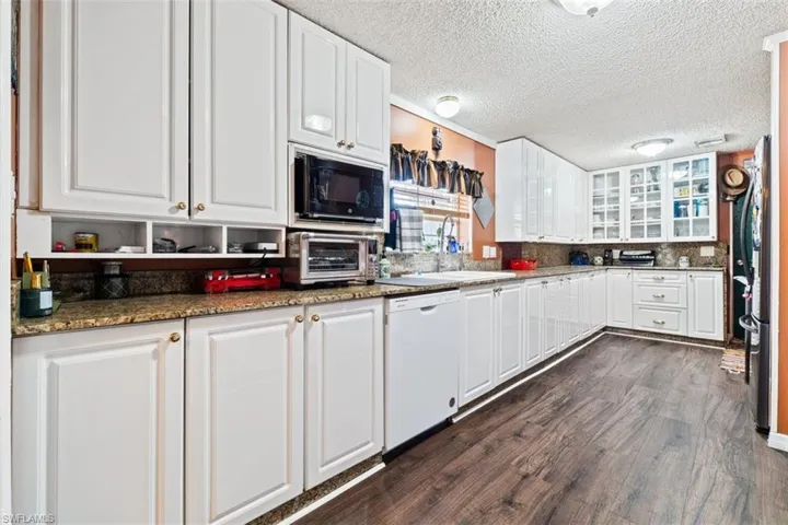 Kitchen featuring white cabinetry, dark stone countertops, white dishwasher, dark wood finished floors, and a textured ceiling