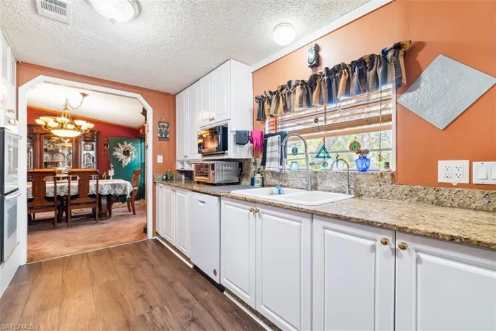 Kitchen with dark wood-type flooring, white cabinetry, light stone counters, a textured ceiling, and white dishwasher