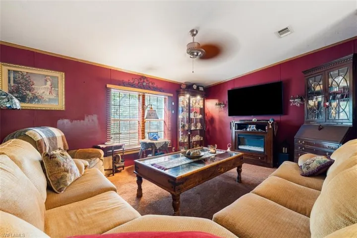 Living room with carpet floors, ceiling fan, crown molding, and lofted ceiling