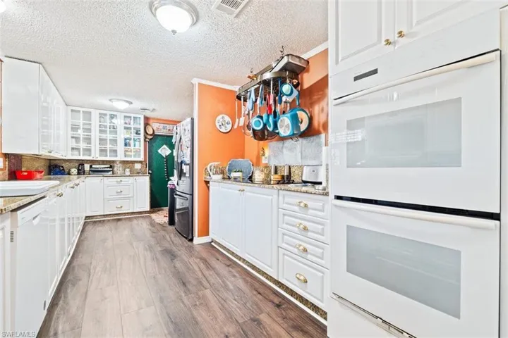 Kitchen featuring white appliances, white cabinetry, glass insert cabinets, dark wood-type flooring, and light stone countertops