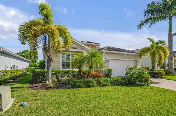 View of front of home with a garage and beautifully manicured front lawn and mature palm trees