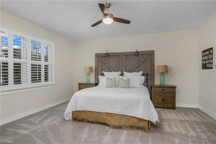 Master carpeted bedroom featuring ceiling fan and plantation shutters