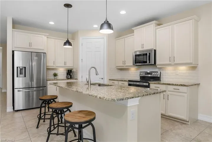 Kitchen featuring tumble tile  backsplash, light tile patterned floors, sink, new in 2024 appliances with stainless steel finishes, and a center island with sink