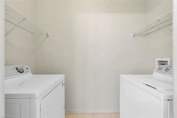 Laundry area featuring light tile patterned floors, baseboards, washing machine and dryer, and laundry area