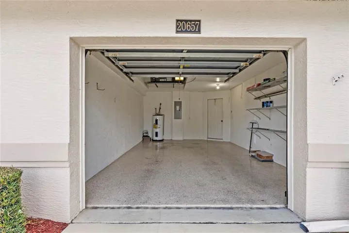 Garage with electric water heater, electric panel, and a textured wall