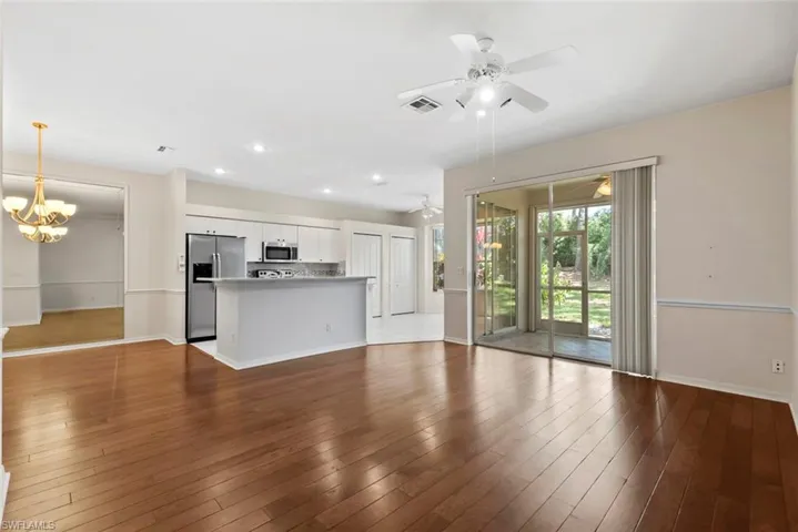 Unfurnished living room with ceiling fan with notable chandelier, wood finished floors, baseboards, and visible vents