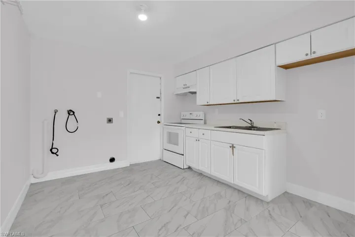 Kitchen featuring white range with electric cooktop, light countertops, white cabinets, and light marble finish floors