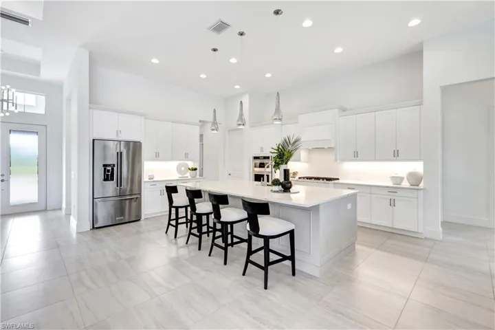 Kitchen featuring appliances with stainless steel finishes, white cabinets, a breakfast bar area, decorative light fixtures, and a large island