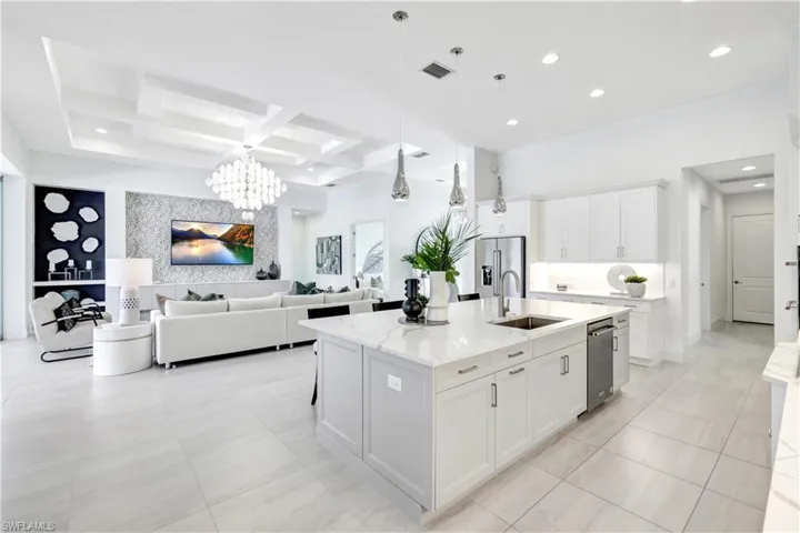 Kitchen featuring white cabinetry, coffered ceiling, decorative light fixtures, a kitchen island with sink, and light stone countertops