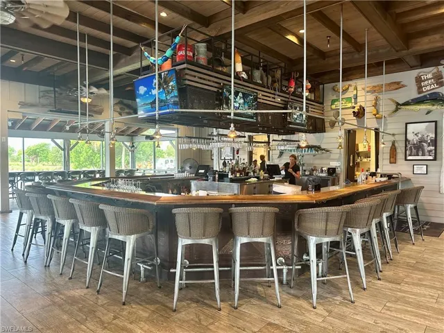 Community bar area with light wood-style flooring, a wood ceiling with exposed beams, decorative light fixtures, and wood walls