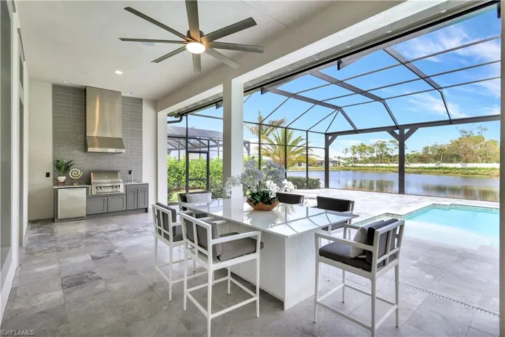 View of patio featuring an outdoor kitchen, a sunroom, a water view, a ceiling fan, and glass enclosure