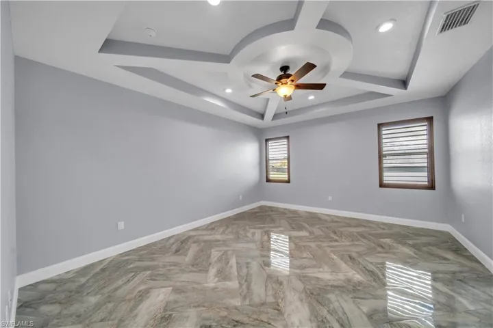 Unfurnished room featuring a raised ceiling, visible vents, ceiling fan, baseboards, and recessed lighting